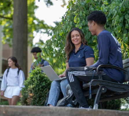 a young caucasian woman and a young African-American man sitting on a bench outside Buchtel Hall